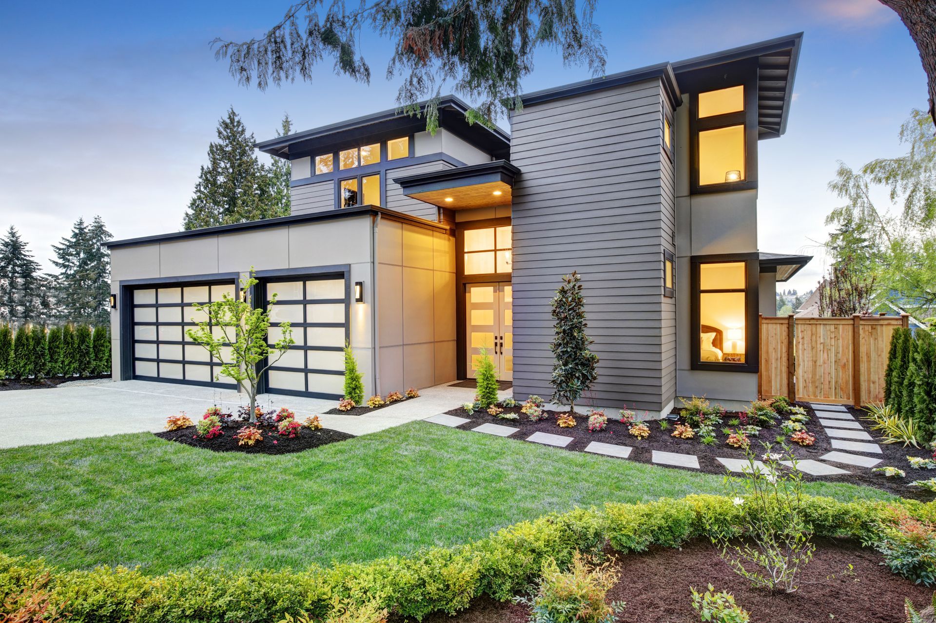 Maison moderne avec garage, fenêtres et pelouse soignée. Façade grise, boiseries noires et allée en pierre.