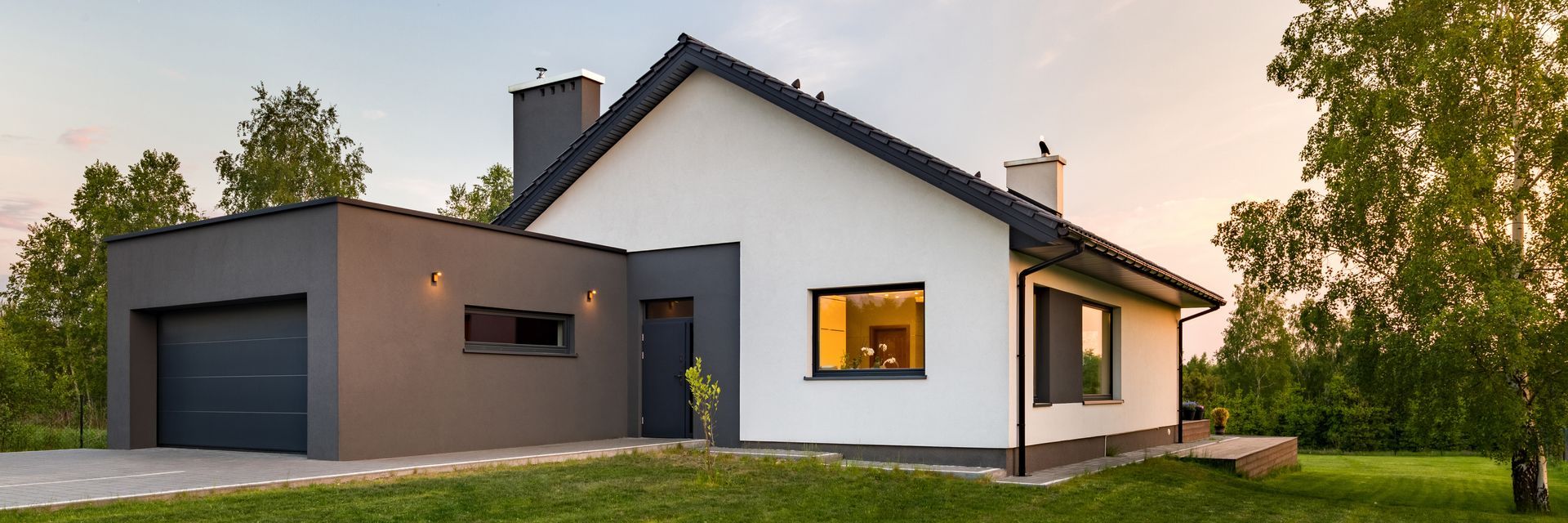 Maison blanche moderne avec garage gris foncé, pelouse verte et arbres.