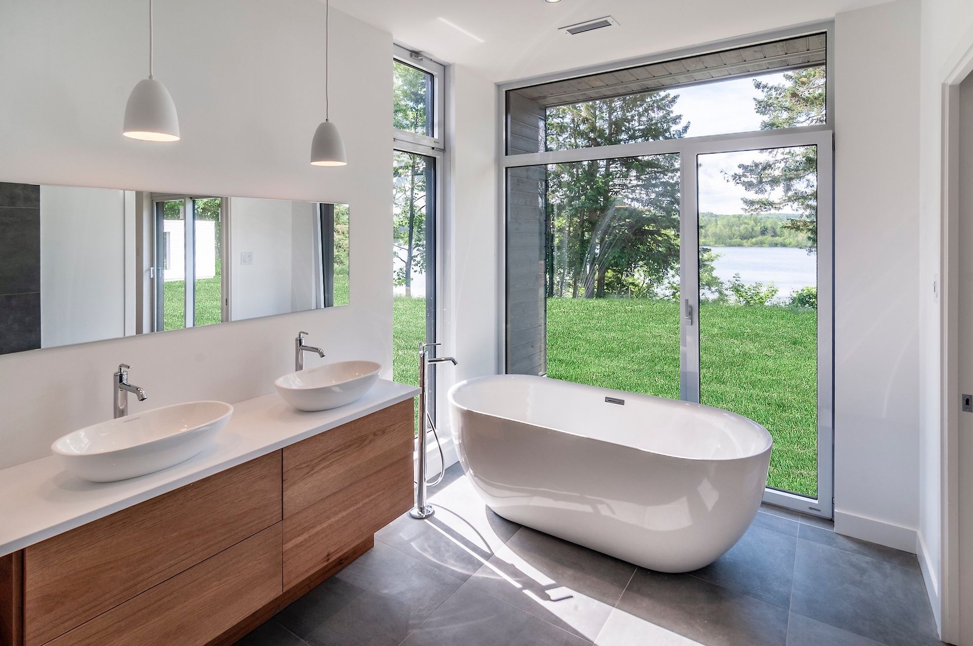 Salle de bains moderne avec baignoire et double vasque donnant sur un lac à travers de grandes fenêtres.