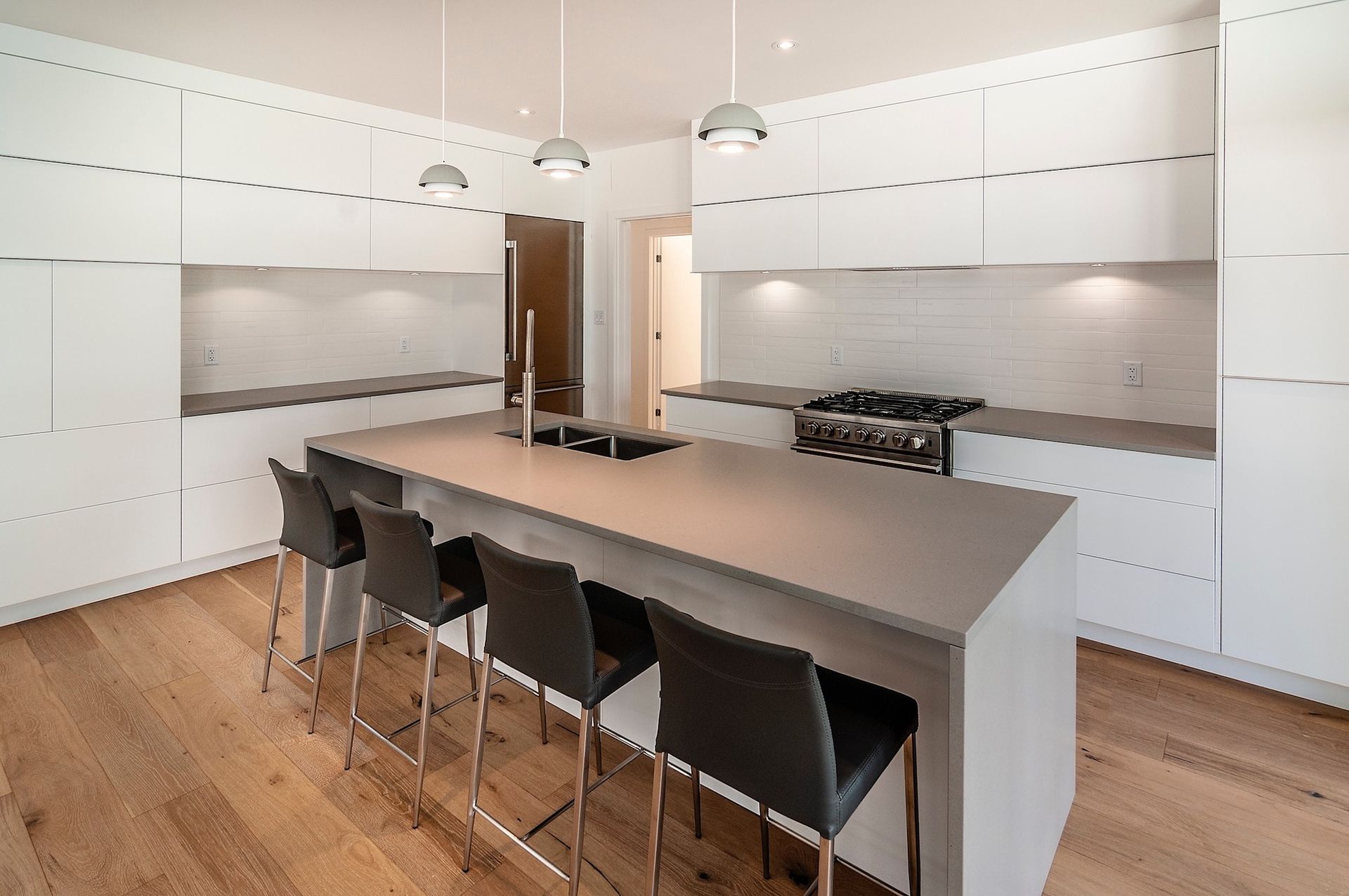 Cuisine moderne blanche avec îlot central, comptoirs gris, tabourets de bar et parquet.