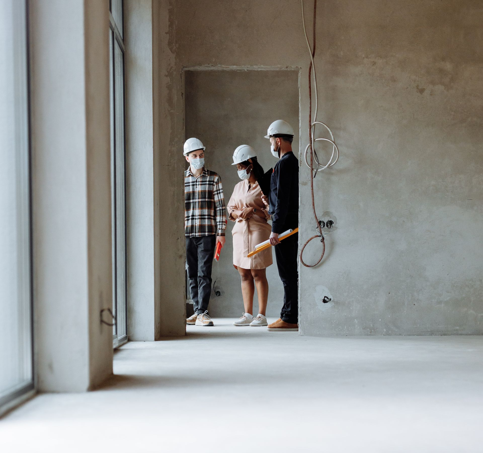 Des ouvriers du bâtiment, casqués et masqués, examinent des plans dans un bâtiment en construction.