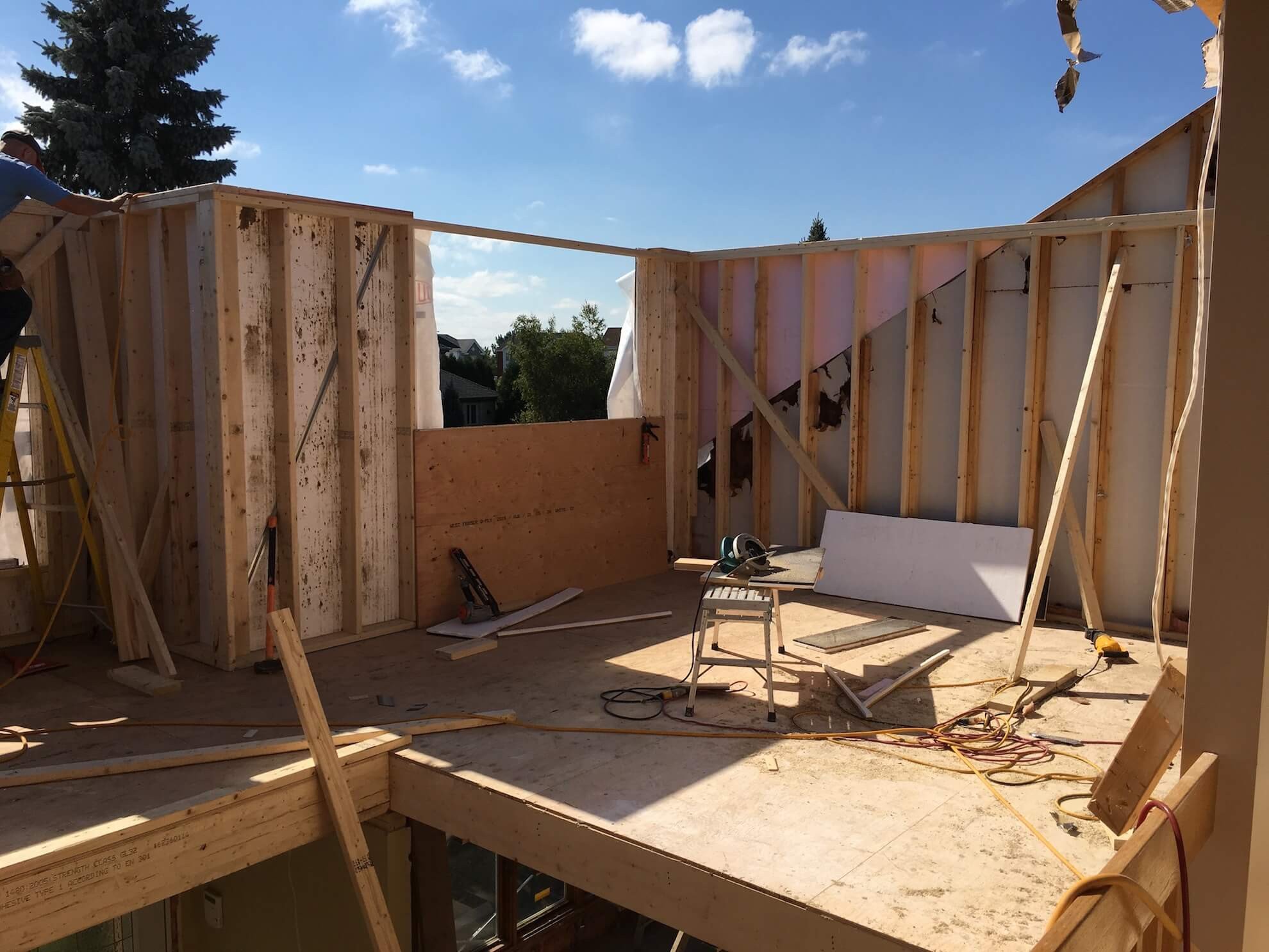 Murs à ossature bois d'une extension de bâtiment en construction, avec un revêtement extérieur partiel en contreplaqué et des montants muraux apparents.