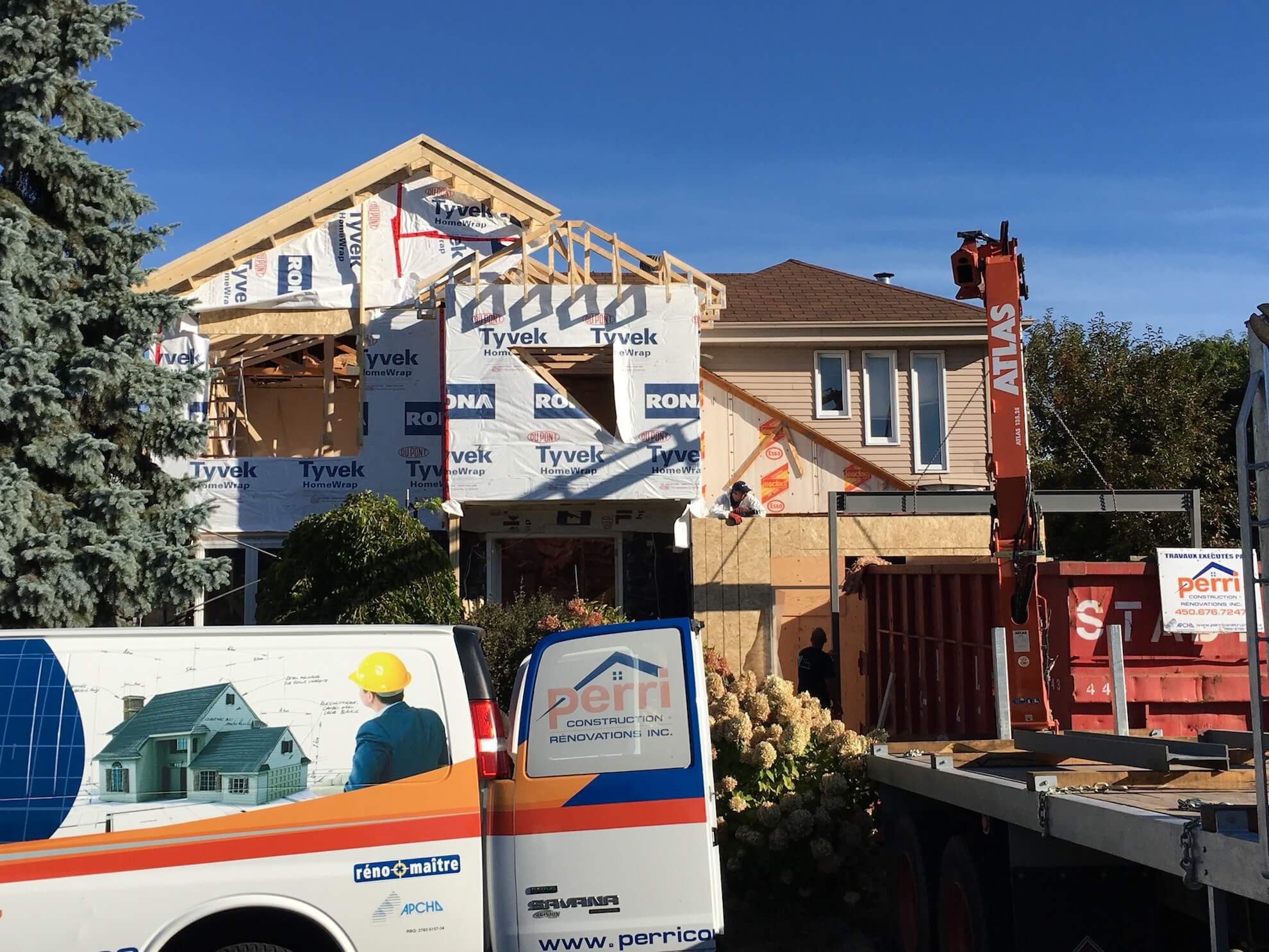 Un chantier de construction montrant une maison en cours de rénovation, avec un camion de chantier de marque Perri et une grue Atlas présents.