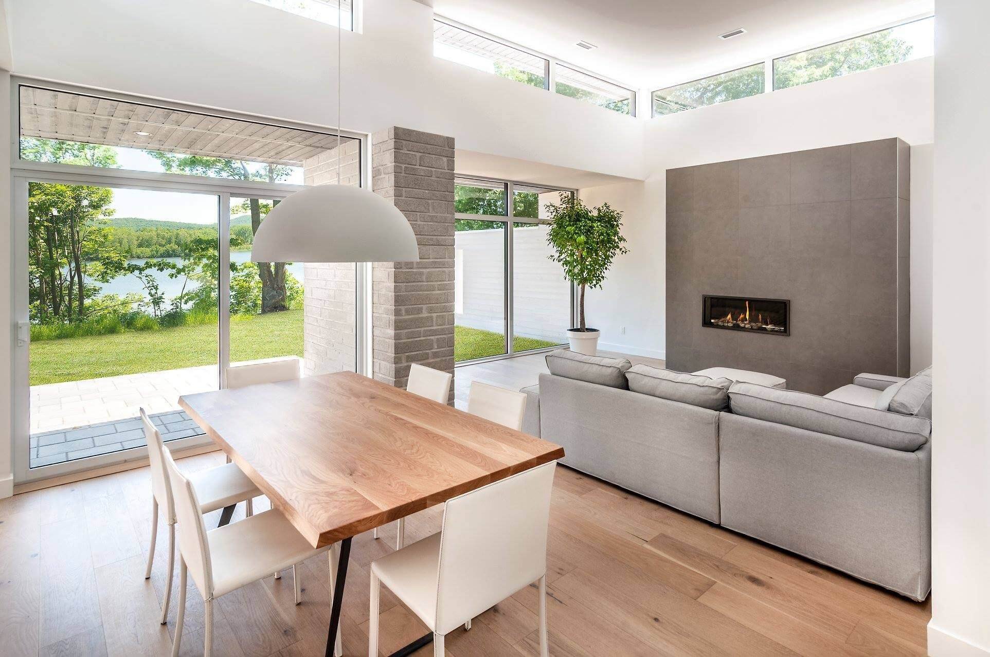 Salon moderne avec coin repas, cheminée et vue sur le lac.