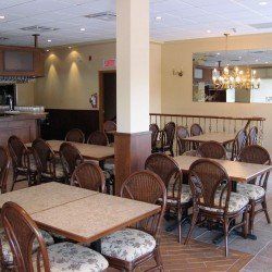 Salle à manger de restaurant avec tables, chaises et lustre. Murs beiges, sièges en bois et osier.
