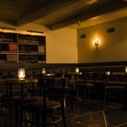 Intérieur de bar faiblement éclairé avec étagères, tables, chaises et bougies.