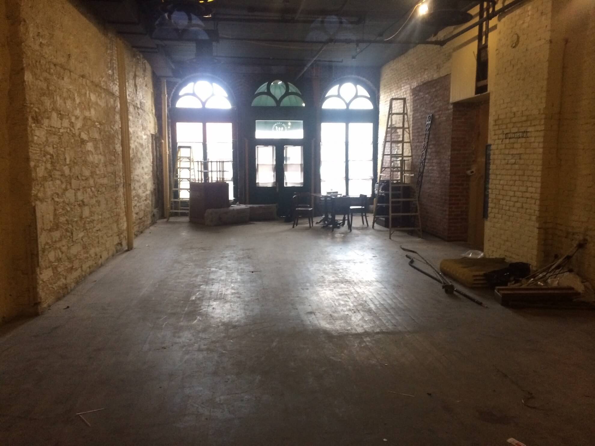 Int&eacute;rieur vide en r&eacute;novation avec murs de brique, sol b&eacute;ton et grandes portes vitr&eacute;es avec arcs.
