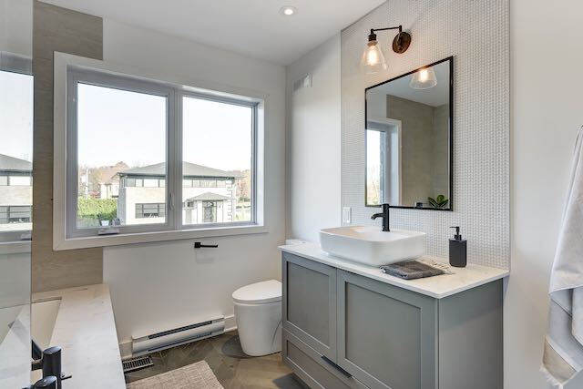 Salle de bain avec vanité grise, miroir rectangulaire, lavabo blanc, fenêtre et murs gris.