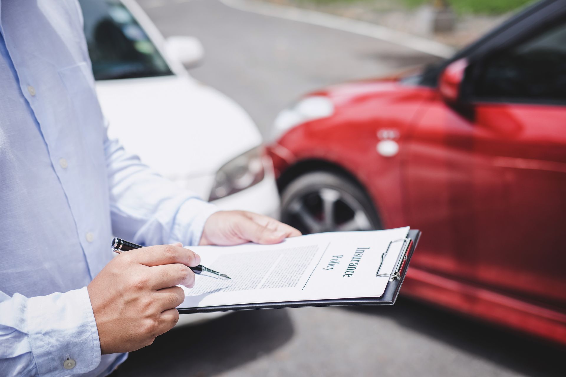 A person reviewing an auto insurance policy on a clipboard near parked vehicles after a collision A person reviewing an auto insurance policy on a clipboard near parked vehicles after a collision