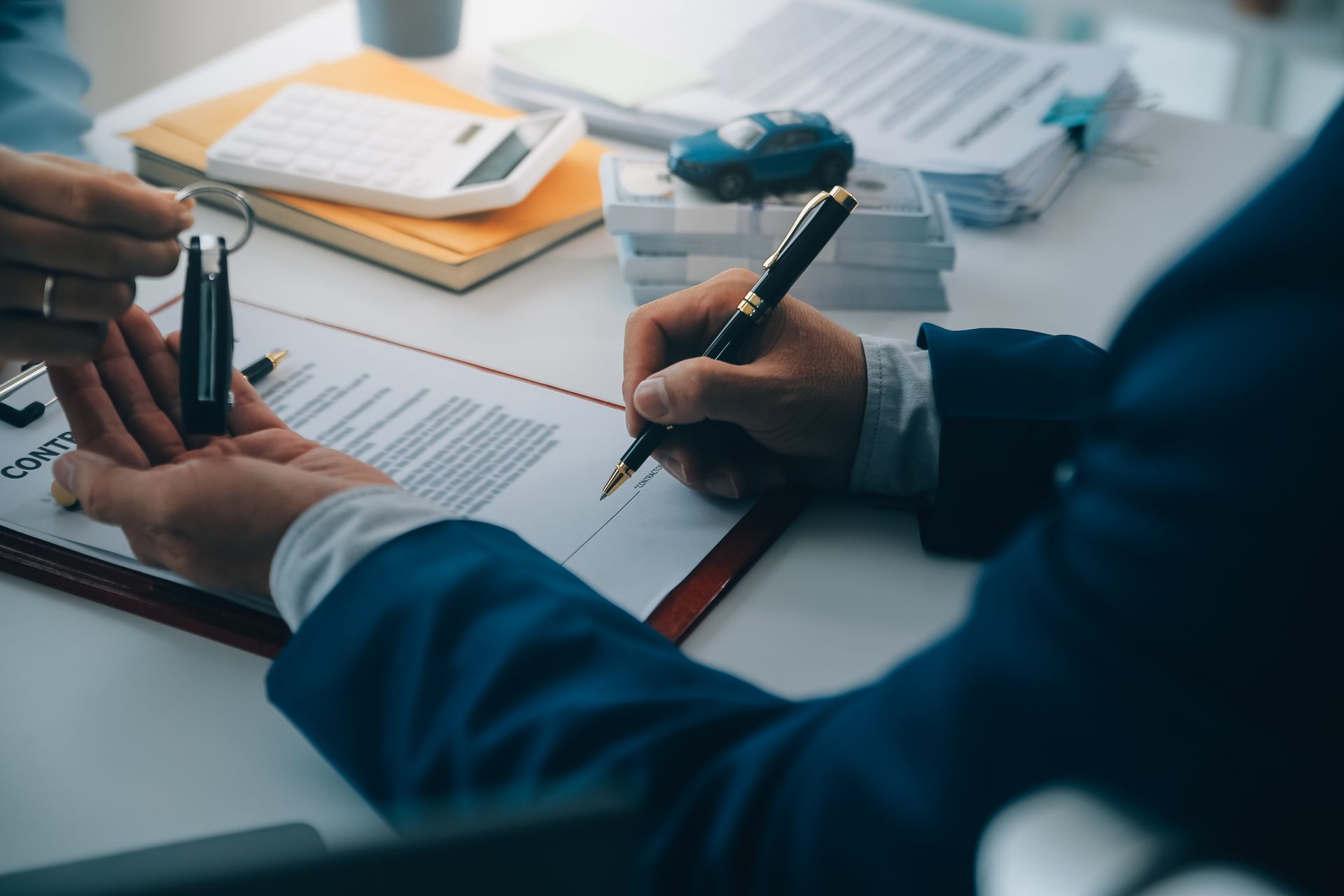 An insurance agent and a client are signing auto policy paperwork at a desk