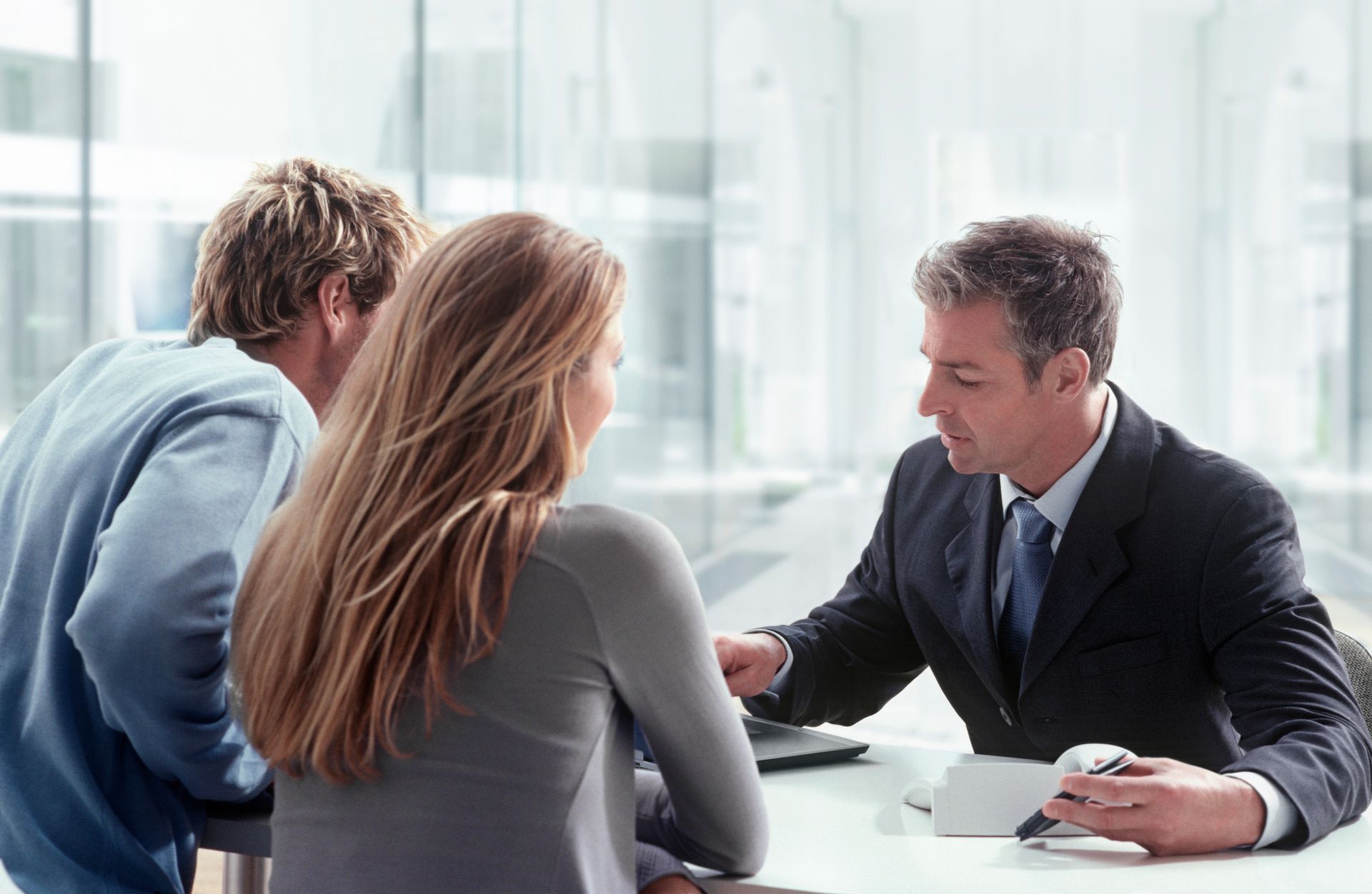 A suited man engages with a man and woman at a table, focusing on general liability insurance.