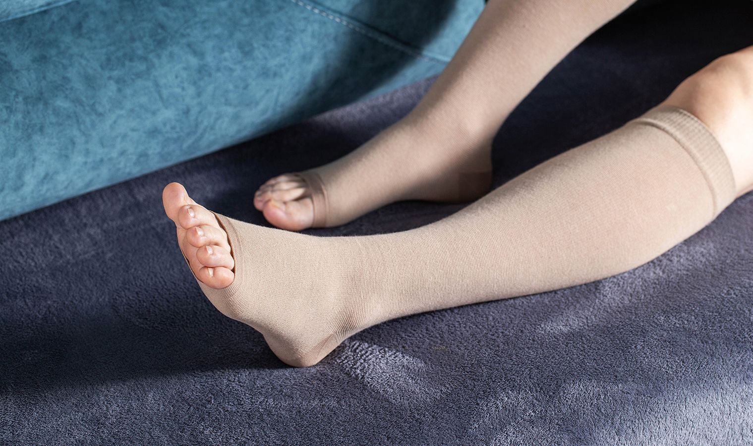 La gamba di una persona, avvolta in una calza compressiva beige, poggia su un divano scuro.