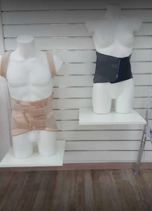 Due manichini in mostra, uno con indosso un indumento modellante beige e l'altro nero, su uno sfondo a doghe bianche.