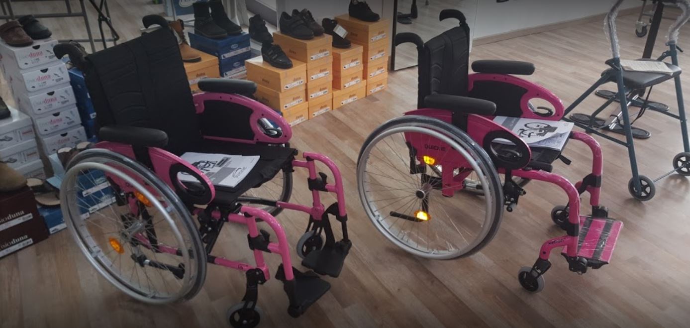 Due sedie a rotelle rosa e nere in una stanza, un deambulatore pieghevole accanto a loro.