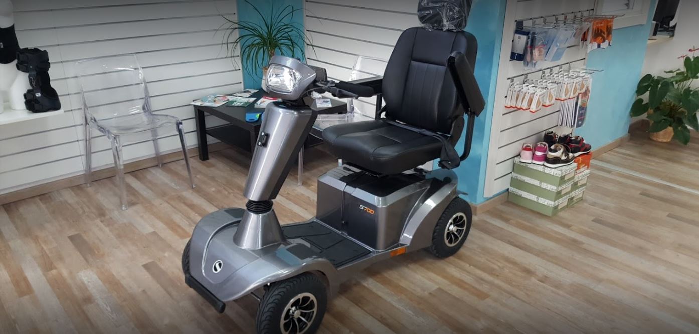 Scooter elettrico nero per disabili con sedile e manubrio in una stanza con pavimento in legno e piante.