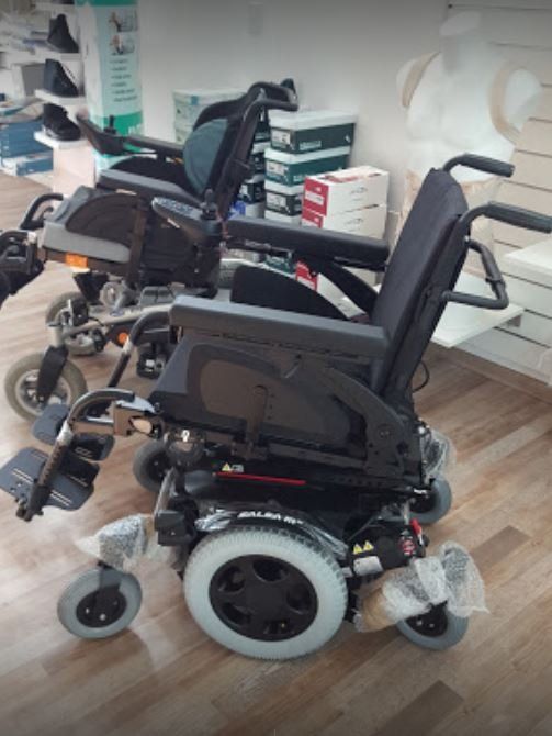 Due sedie a rotelle elettriche nere in uno showroom, una accanto all'altra su un pavimento chiaro.