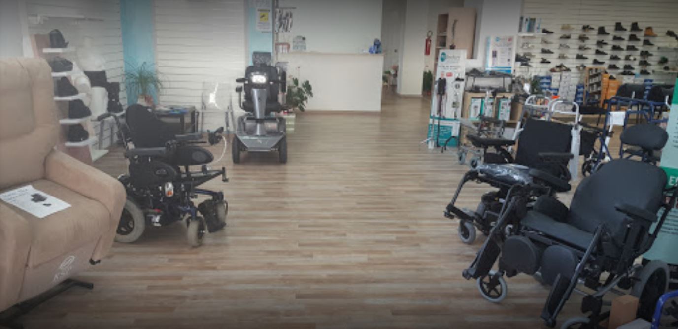 Ausili per la mobilità accessibili esposti in uno showroom luminoso con pavimento in legno e scaffali pieni di attrezzature.