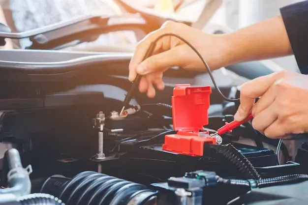 Mechanic connecting a red battery charger to a car engine in an auto repair shop