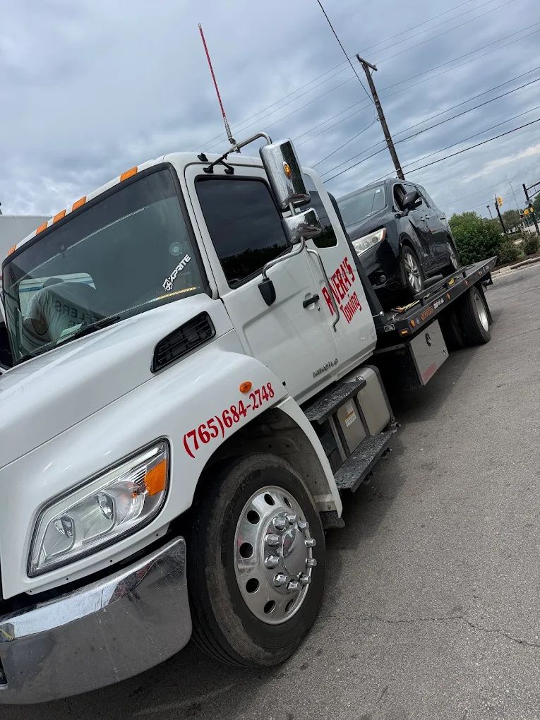 Tow truck carrying a white car on a flatbed beside a grassy roadside