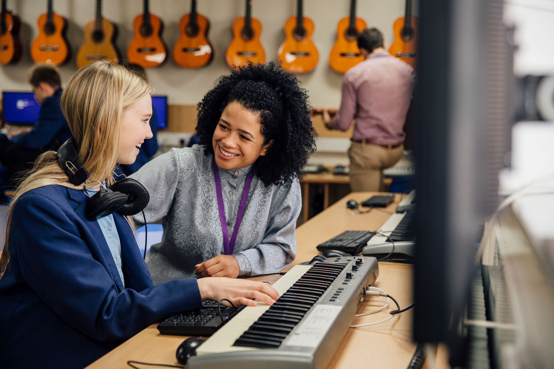 Two people smiling over a keyboard in a music store with guitars hanging on the wall