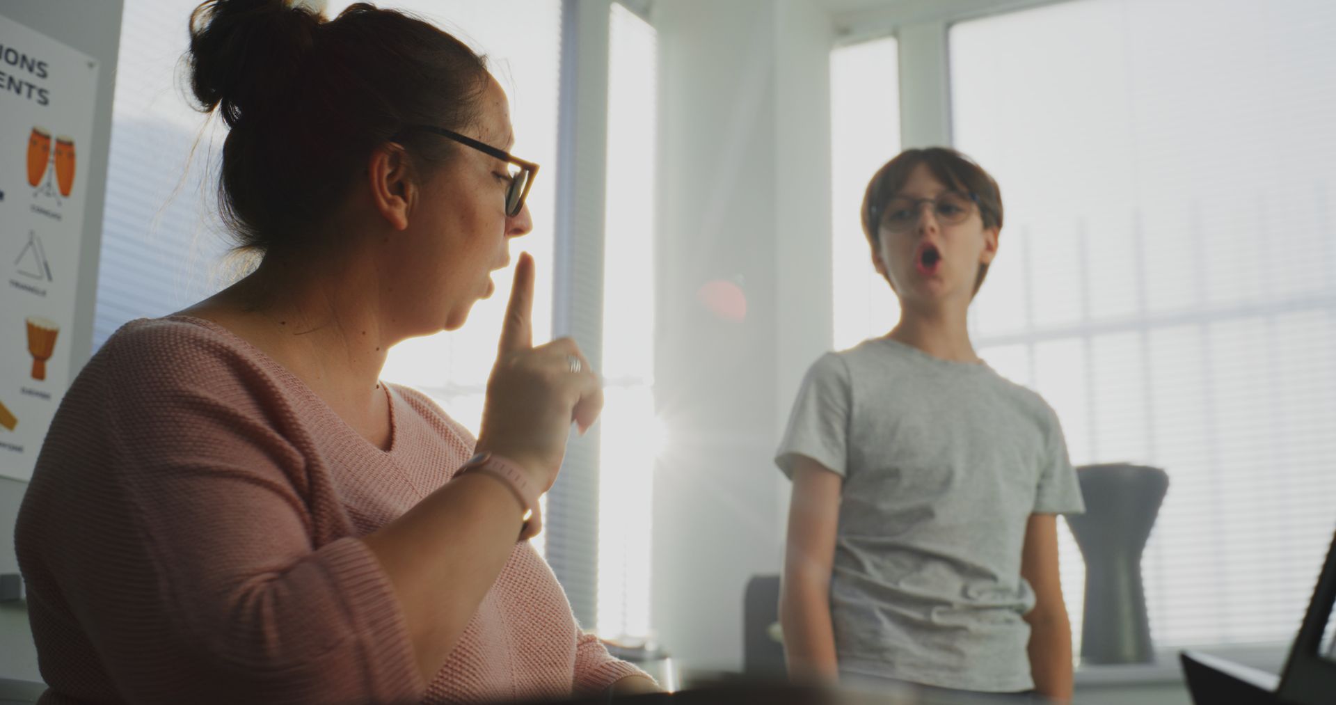 Two people talking in a bright office; one gestures while seated, the other stands nearby. Two people talking in a bright office; one gestures while seated, the other stands nearby.