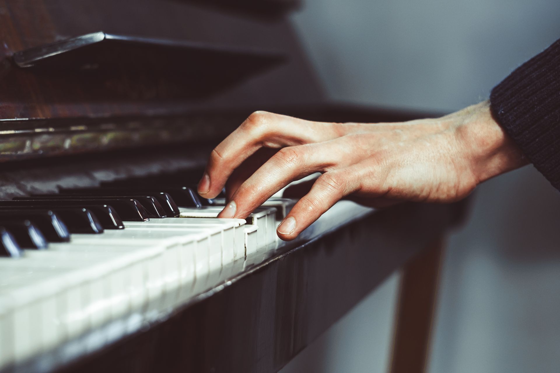 Hand playing white piano keys on a black piano in soft light Hand playing white piano keys on a black piano in soft light