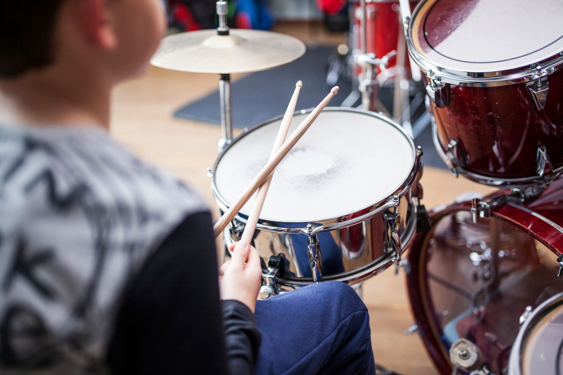 Drummer playing a snare drum with sticks beside a red drum kit Drummer playing a snare drum with sticks beside a red drum kit