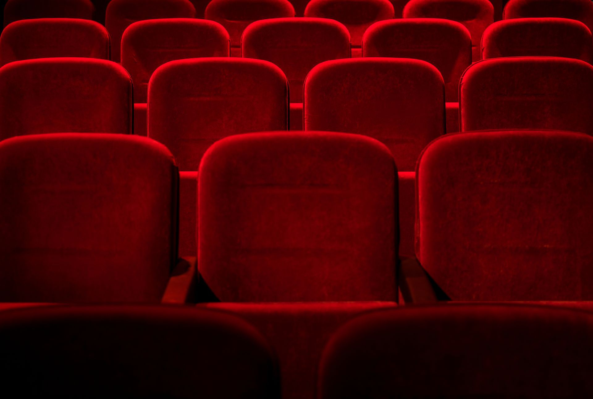 Rows of empty red theater seats in a dimly lit auditorium