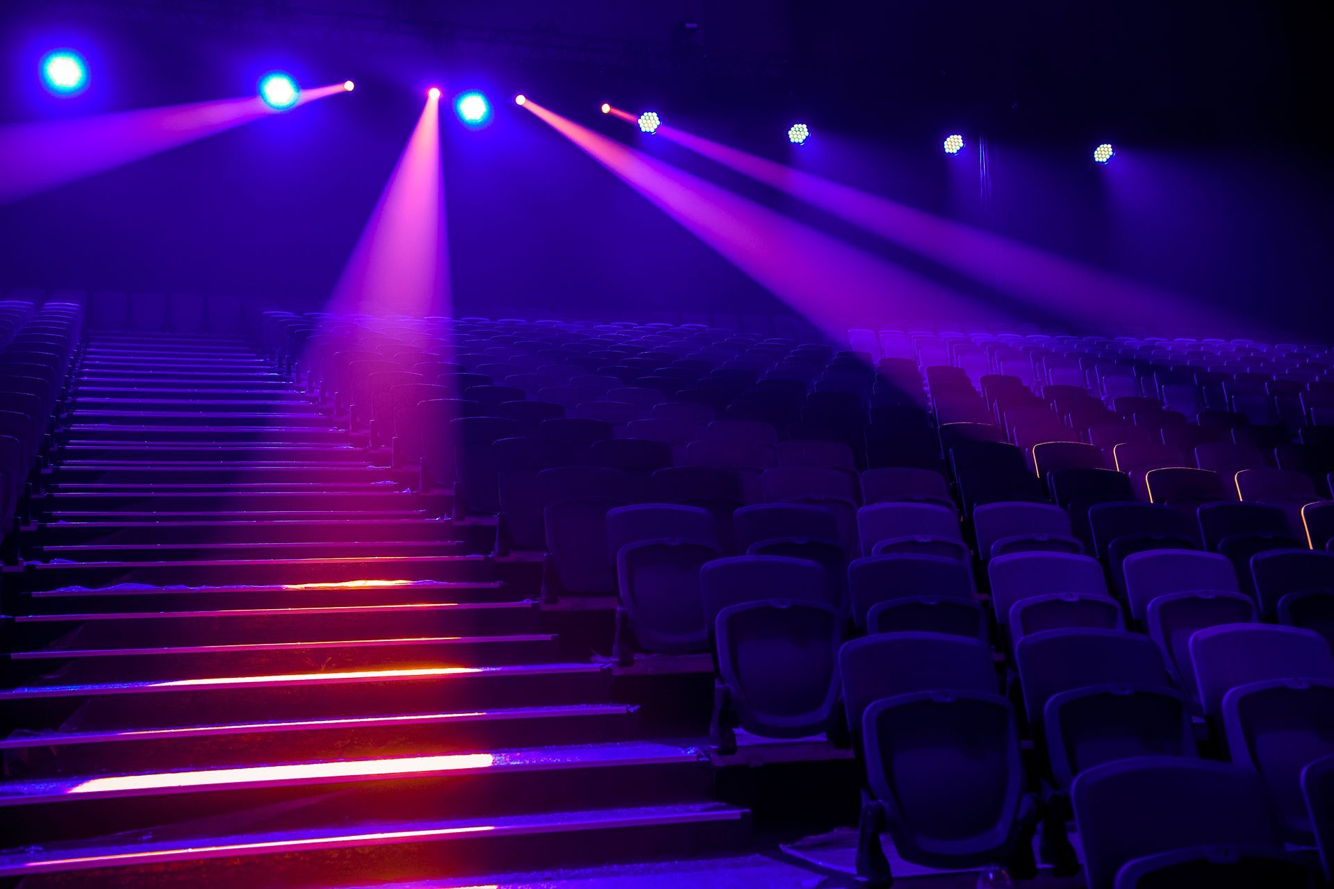 Empty theater seats under purple stage lights with illuminated stairs Empty theater seats under purple stage lights with illuminated stairs