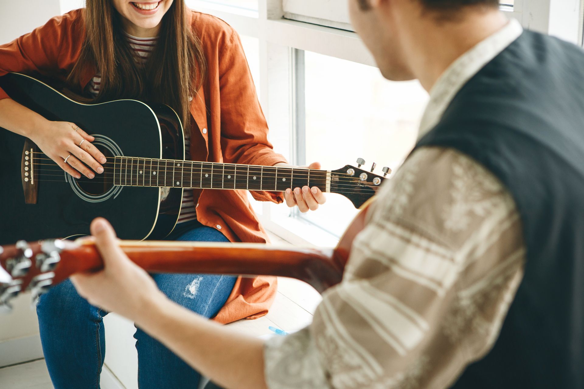 Two people playing acoustic guitars in a bright indoor music lesson