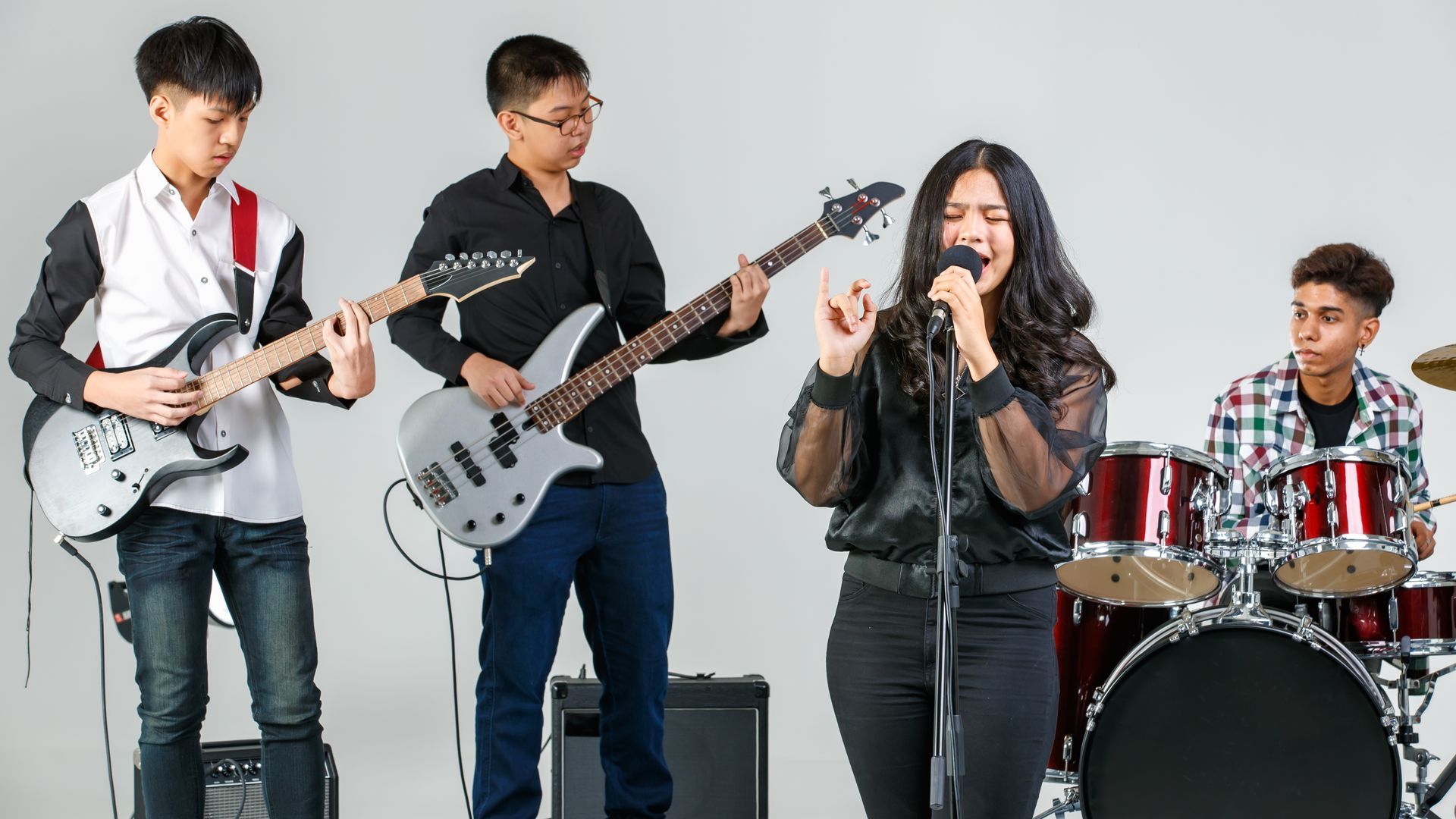 Four musicians rehearsing, with guitars, bass, vocals, and drums against a plain white background