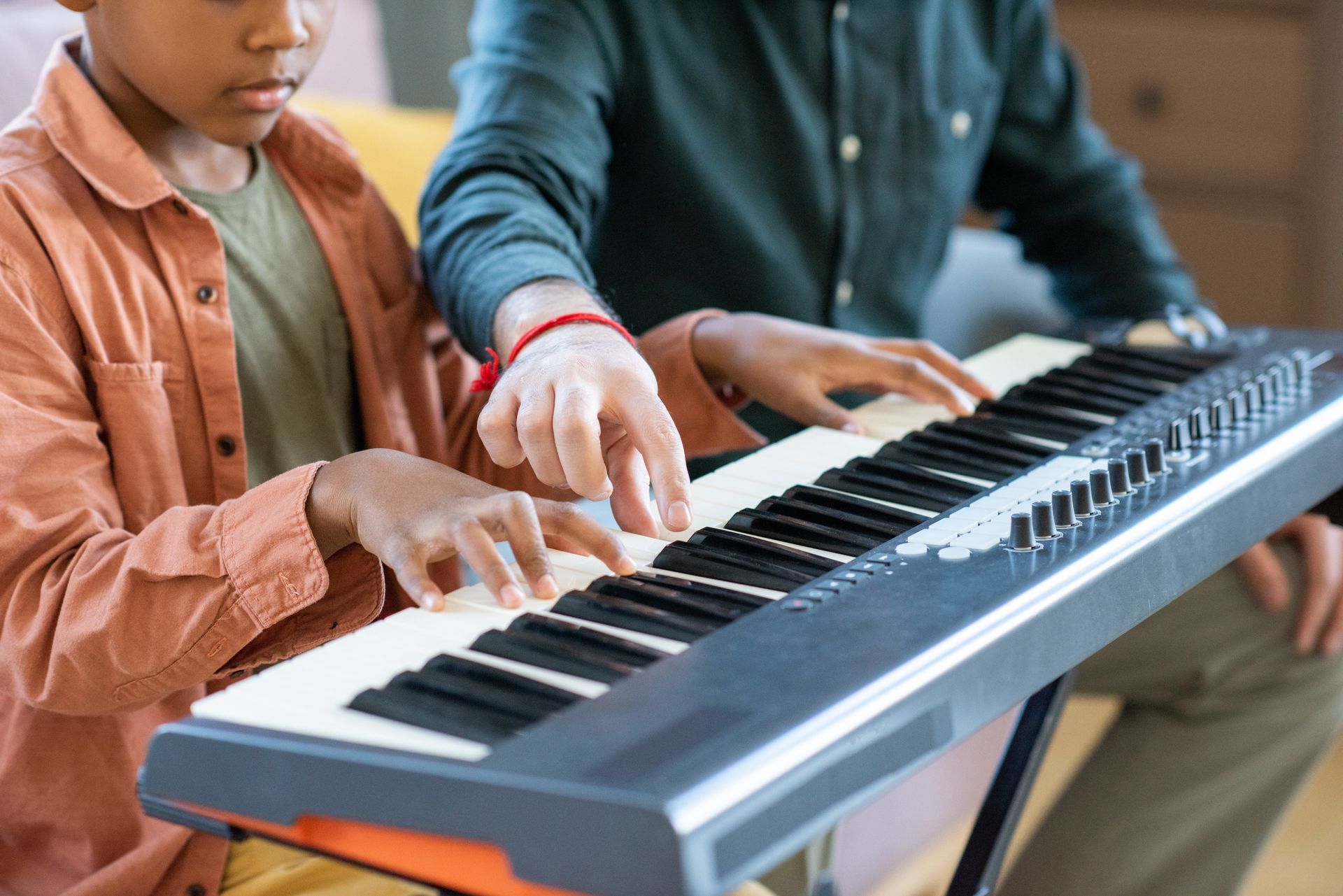 Two people playing a keyboard together, with hands on the keys in a bright indoor setting