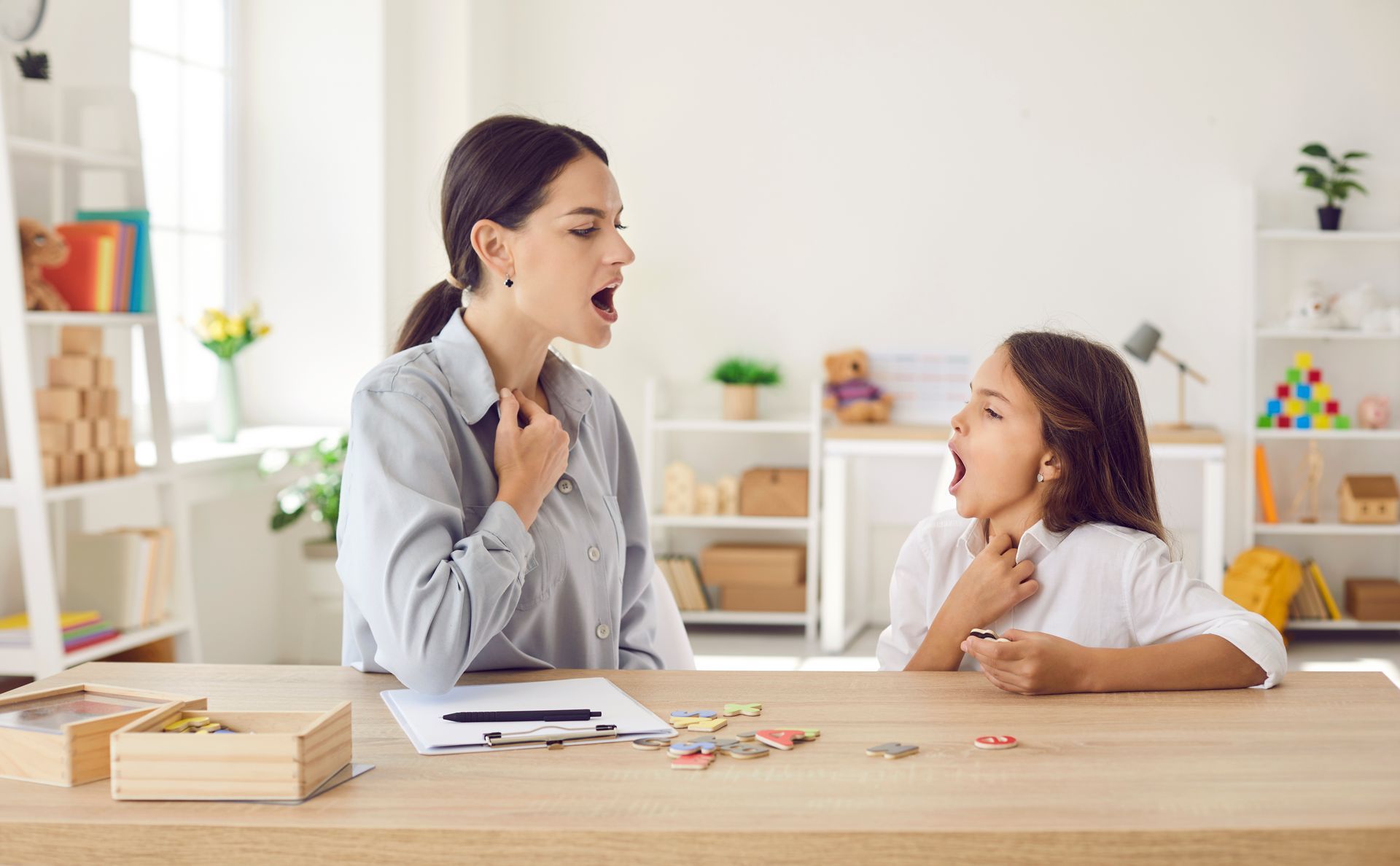 Teacher and child in a bright classroom, talking at a table with books and pencils. Teacher and child in a bright classroom, talking at a table with books and pencils.