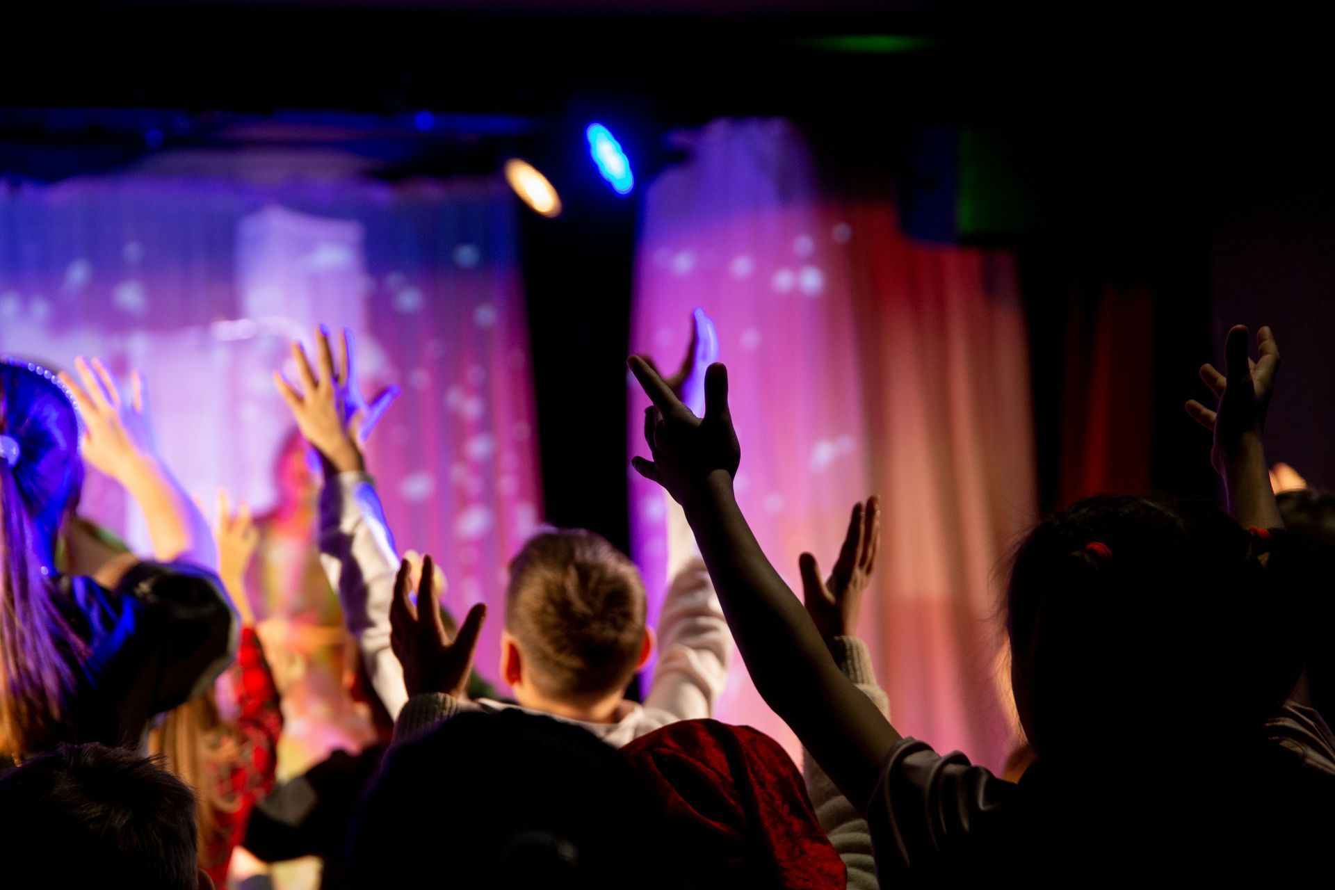 Audience with raised hands at a colorful concert or event stage with purple and pink lighting