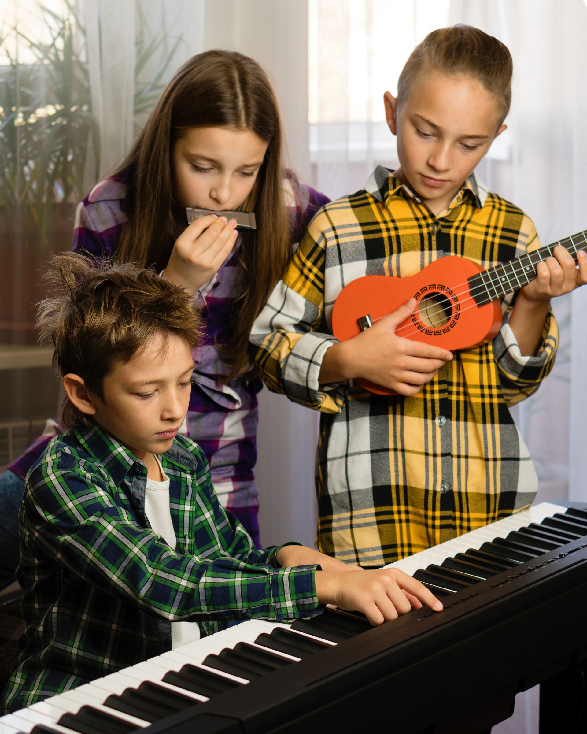 Three children playing keyboard and ukulele while another sings in a bright room.