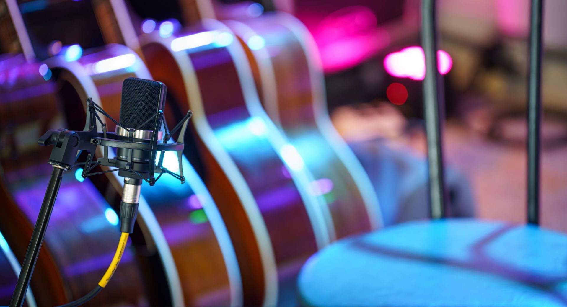 Microphone in front of colorful acoustic guitars on a softly lit stage Microphone in front of colorful acoustic guitars on a softly lit stage
