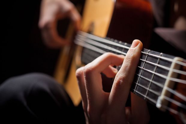 Close-up of hands playing an acoustic guitar, with fingers pressing the strings on the fretboard. Close-up of hands playing an acoustic guitar, with fingers pressing the strings on the fretboard.