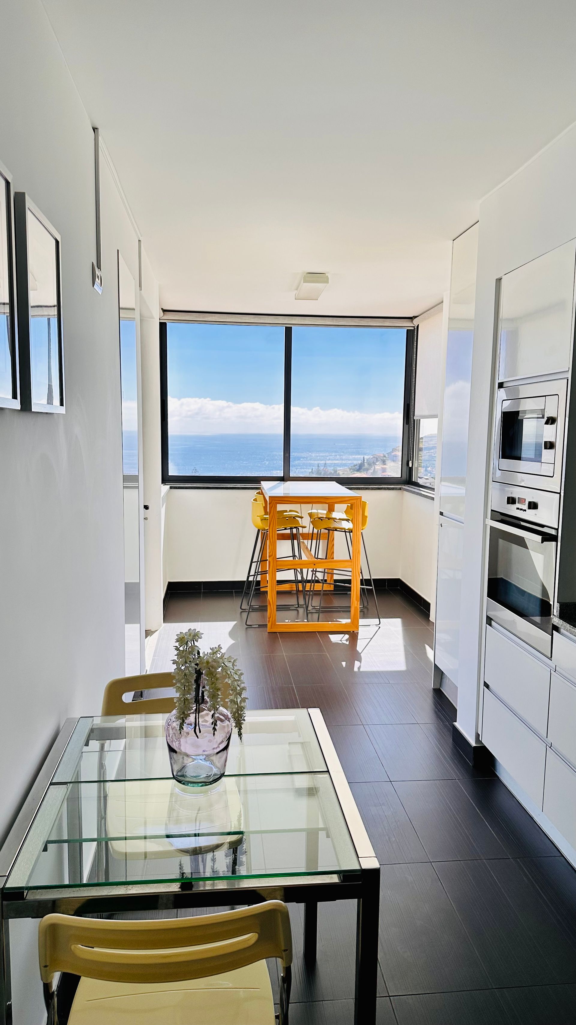 A kitchen with a glass table and chairs and a view of the ocean.