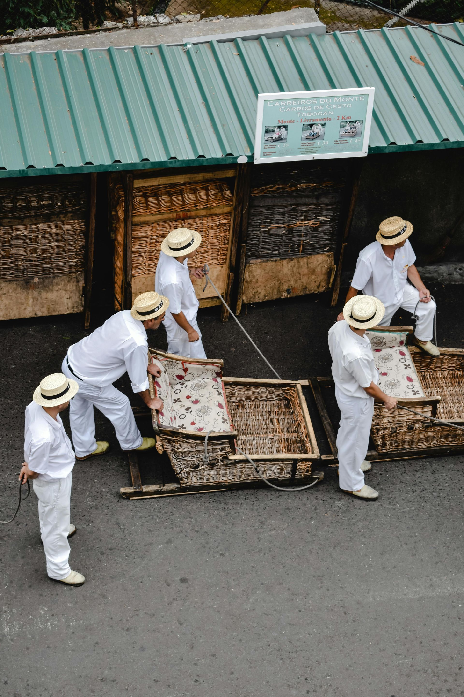 What to do in Madeira: traditional downhill kart. A group of men wearing hats pushing carts down a street.