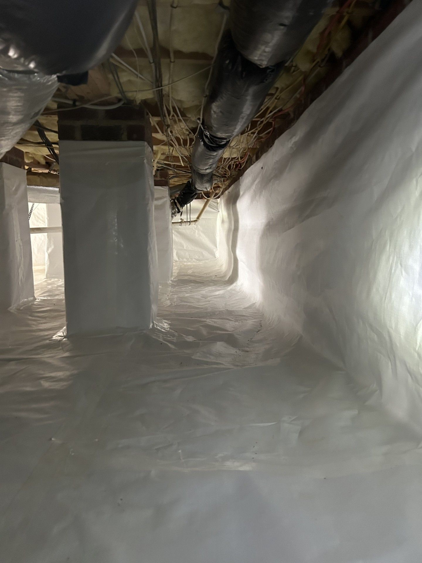 A crawl space filled with plastic and pipes.