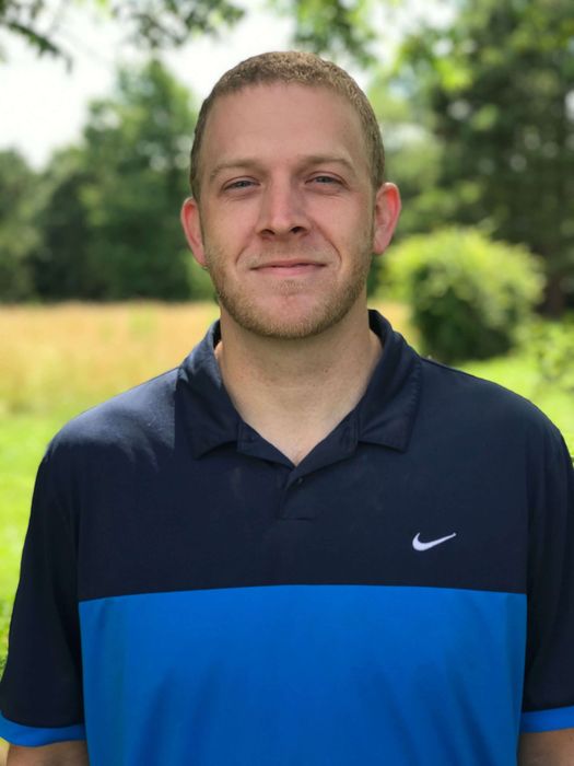 A man wearing a blue and black nike shirt is smiling for the camera.