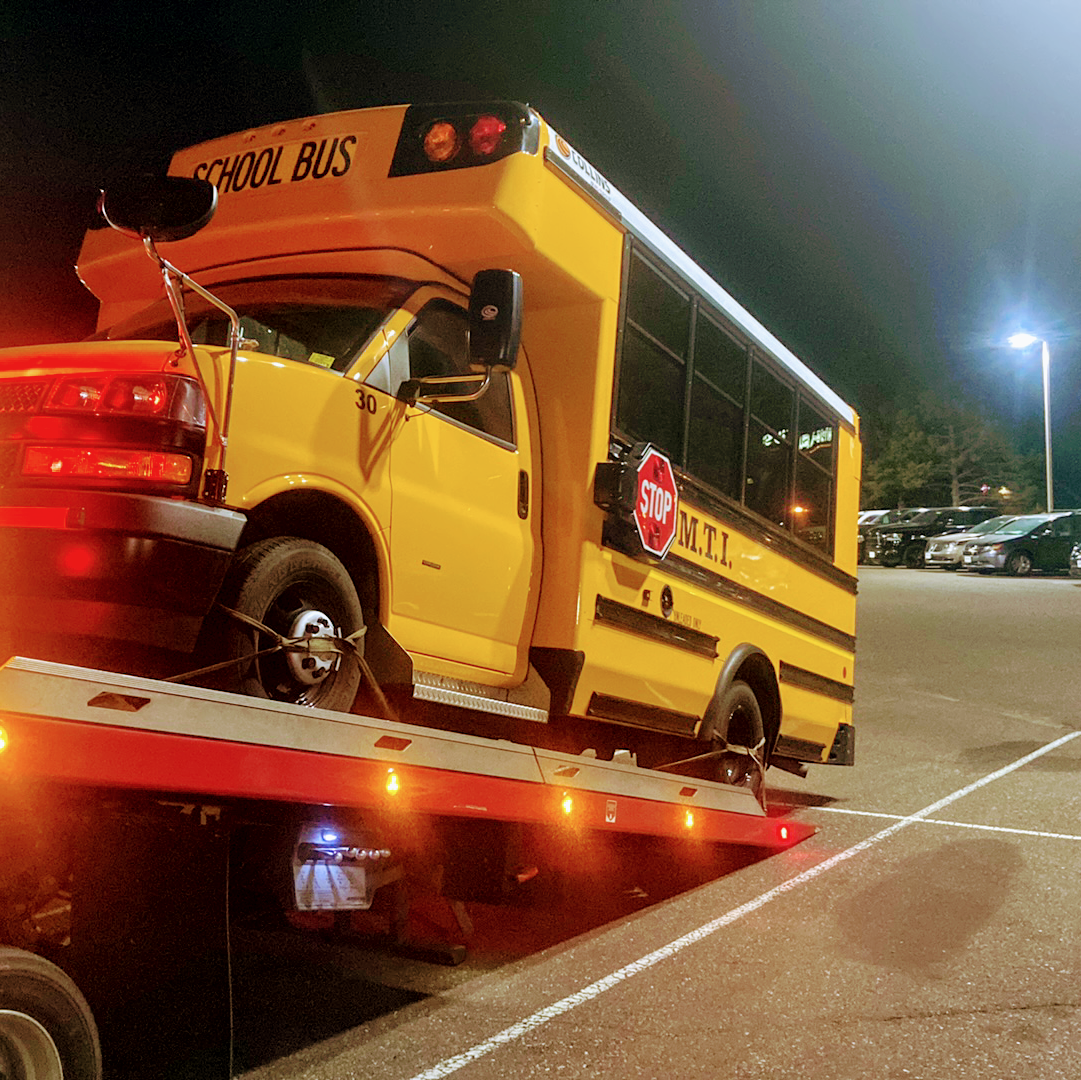 Yellow school bus loaded on a tow truck at night in a parking lot