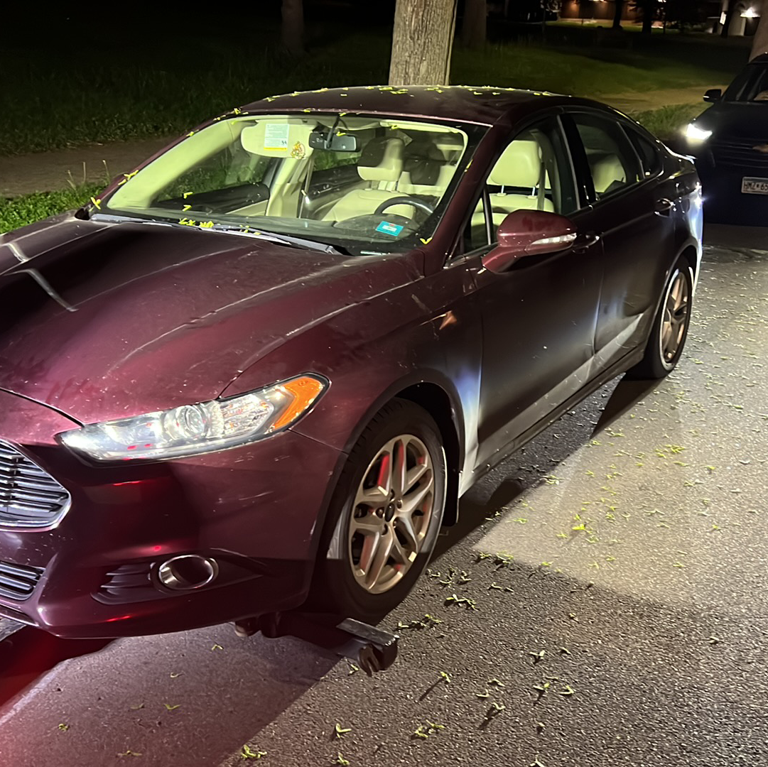Maroon sedan parked at night on a street, viewed from the front-left side.