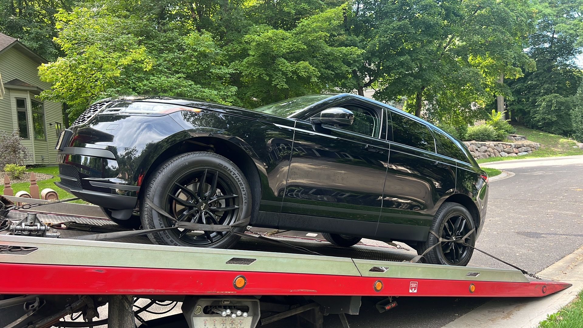 Black SUV on a red tow truck bed on a tree-lined residential street