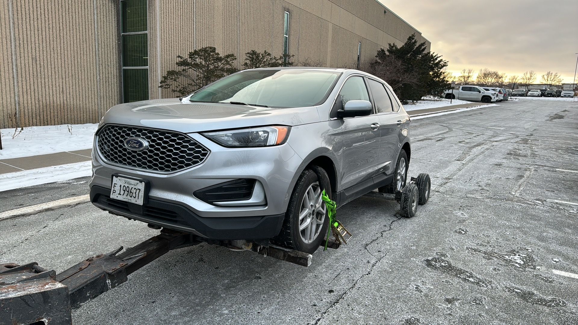 Silver SUV with front-left wheel damaged and tilted on a snowy roadside near a building