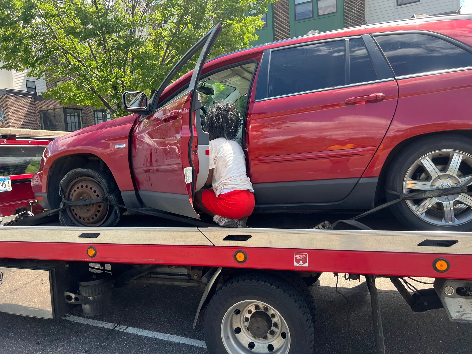 Red SUV on a tow truck with driver door open and a red-and-white plush toy hanging from it.