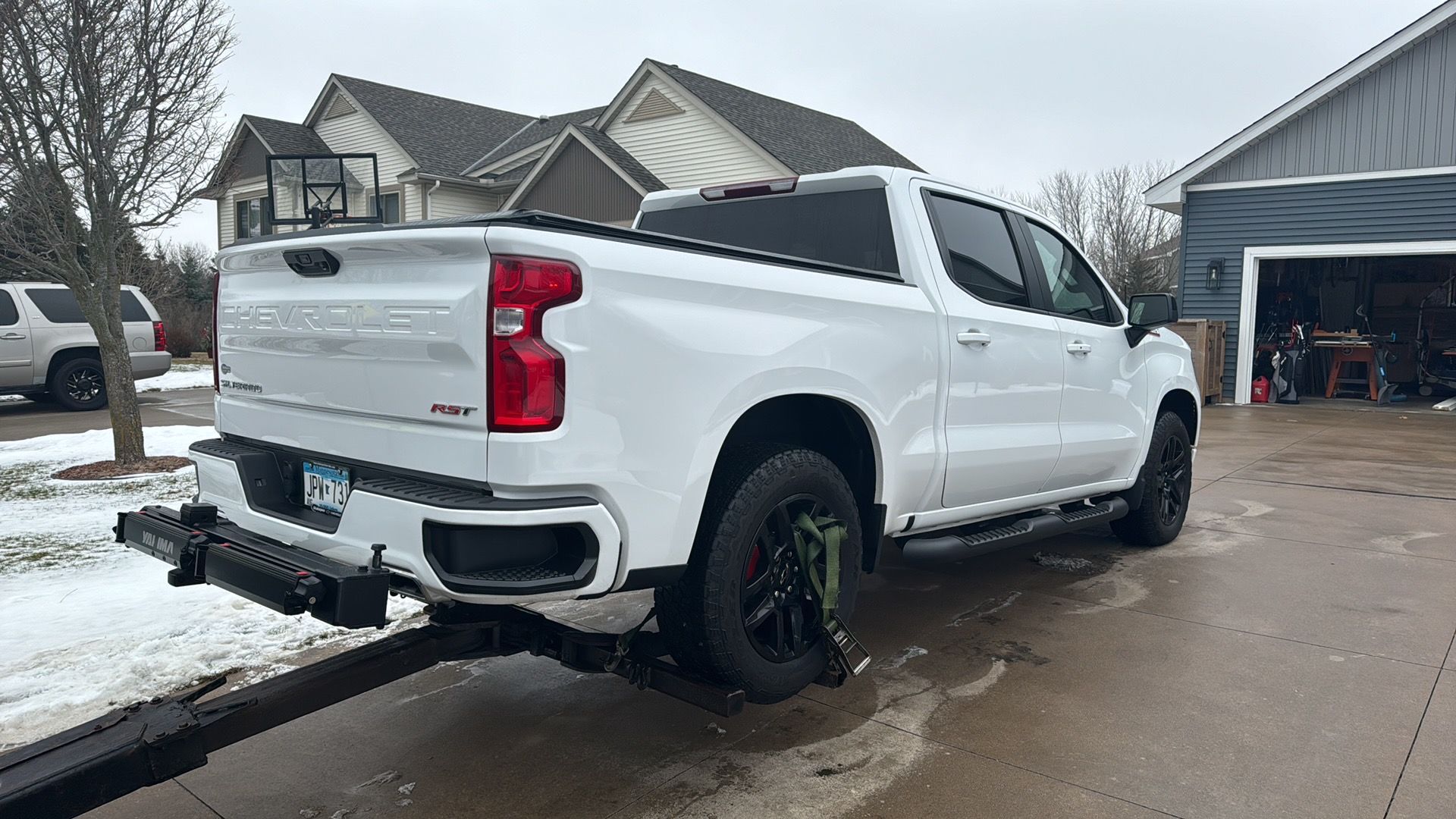 White pickup truck parked on a wet driveway in a snowy suburban neighborhood, rear three-quarter view