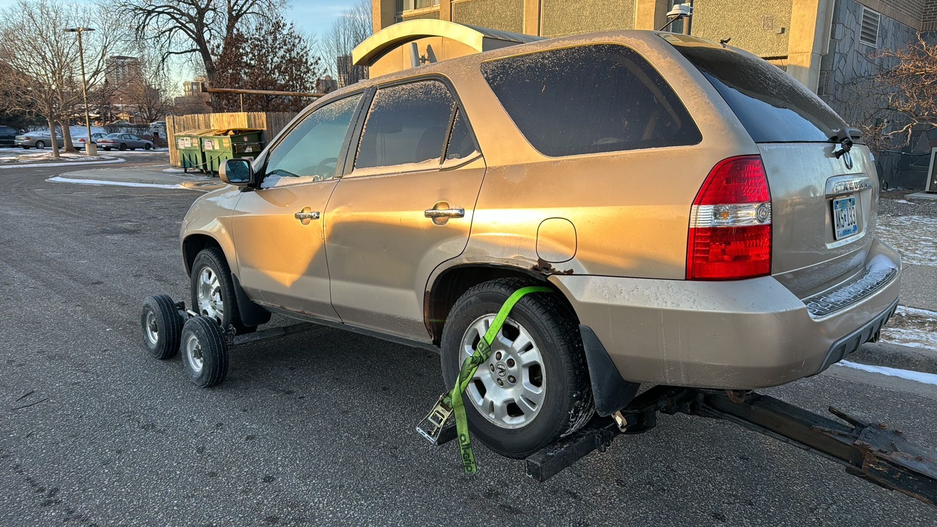 Gold SUV with damaged wheels towing on a trailer in a parking lot.