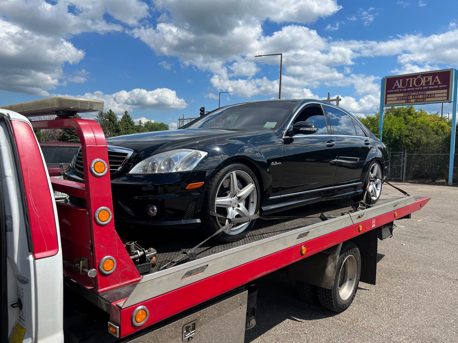Black sports car on a red flatbed tow truck under a blue sky.