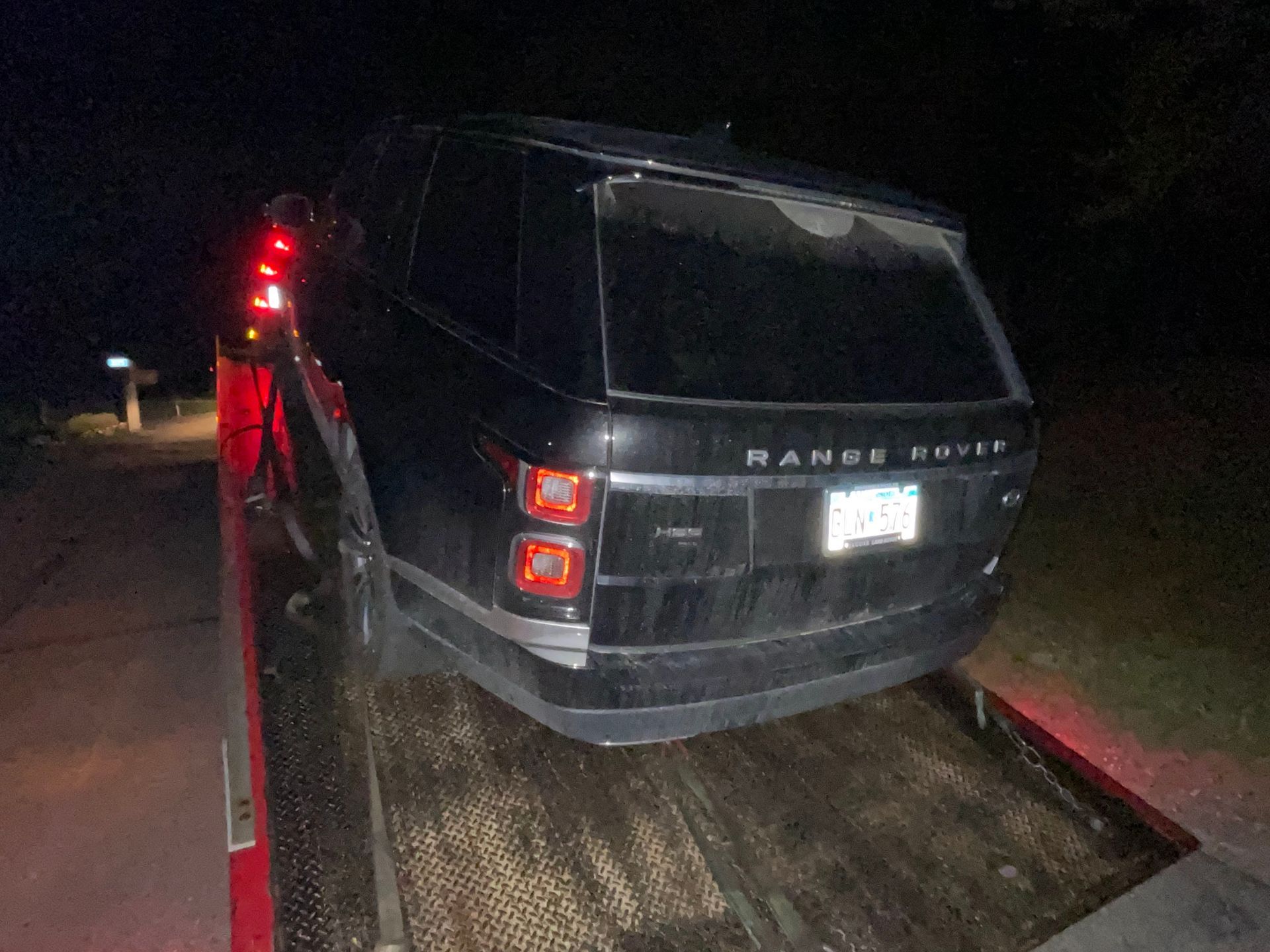 Dark Range Rover on a tow truck at night, lit by red taillights.